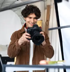 Happy photographer guy taking professional photos of various desserts in modern photostudio, using digital camera