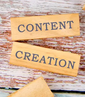 Two wooden blocks on a distressed table, one reading "CONTENT" and the other "CREATION."